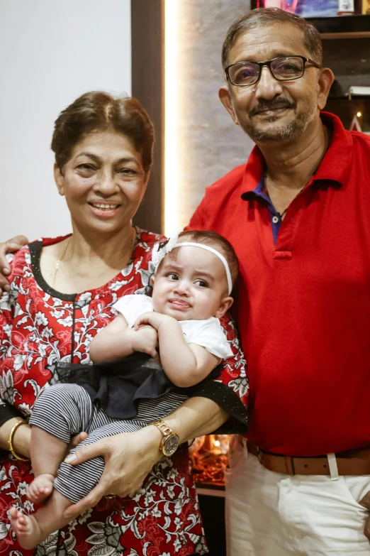 an older man and woman holding their baby in front of a television