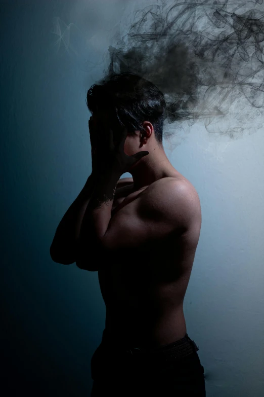 man wearing black underwear and smoking cigarette behind a dark background