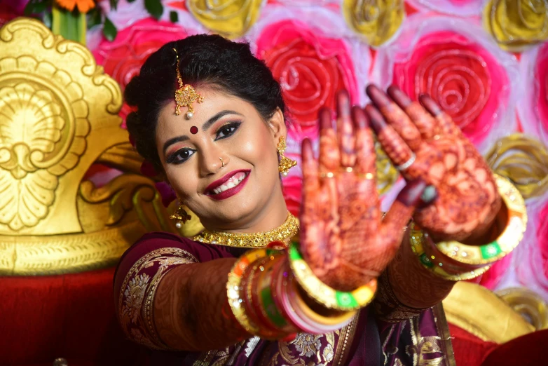 a smiling woman in traditional indian wear has her hands outstretched