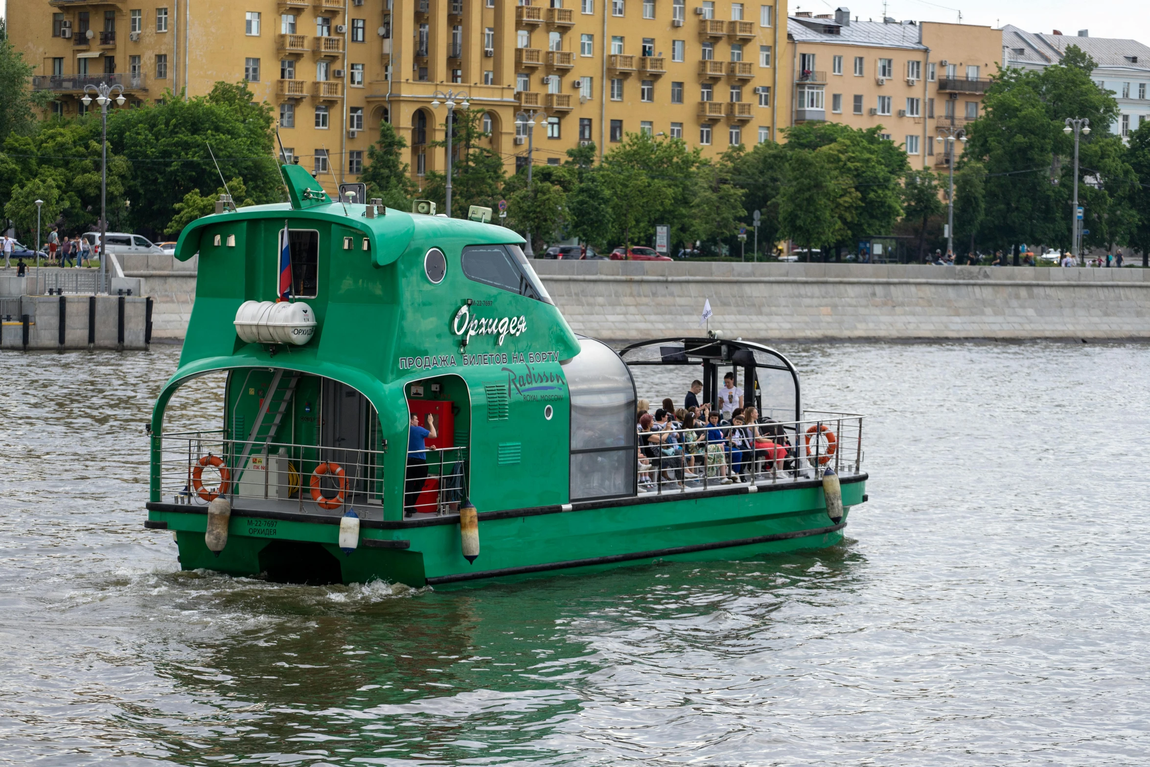 green tour bus on the river near buildings