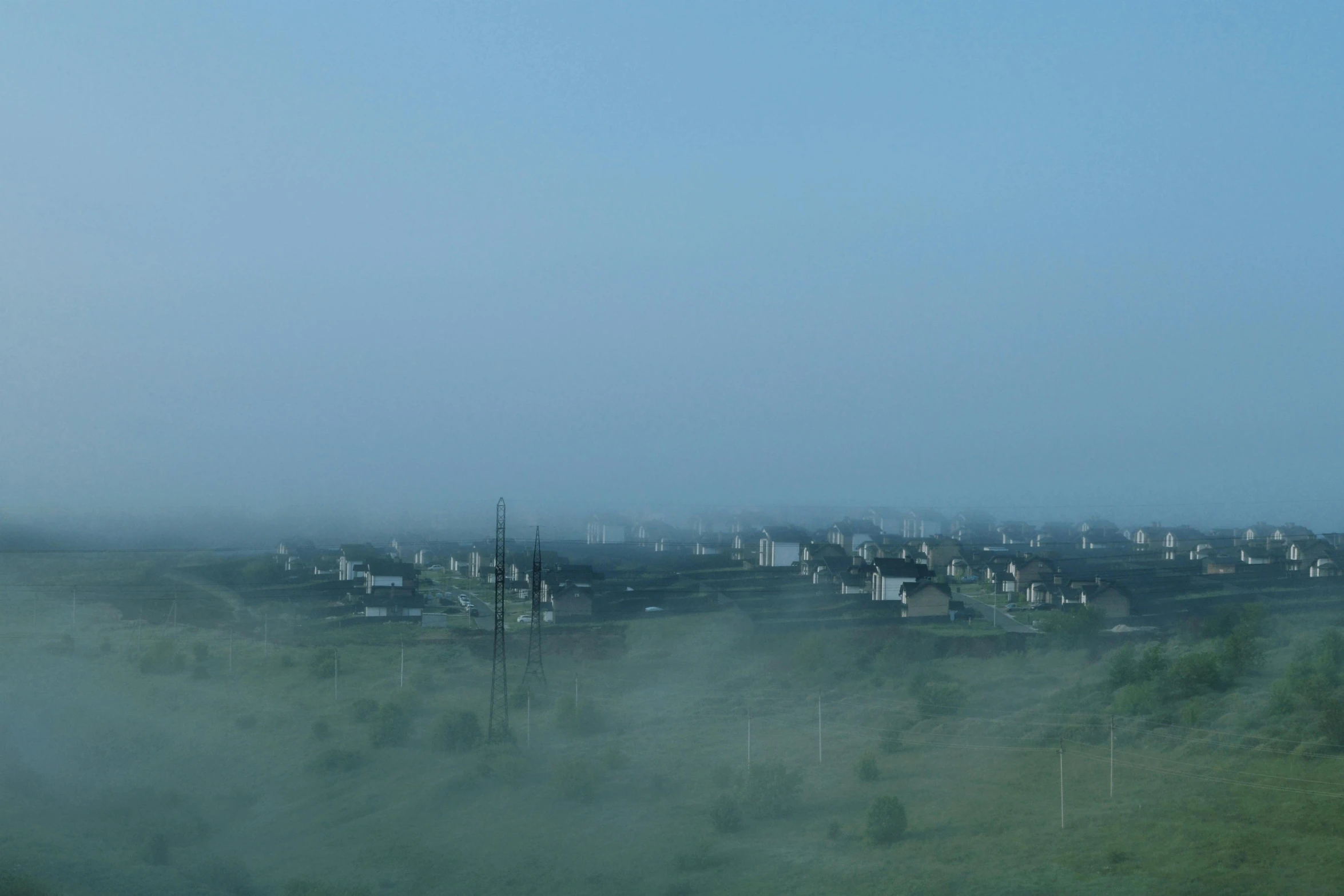 fog rises as homes sit alone in a green field