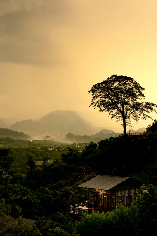 a foggy sky and clouds with a lonely tree and house