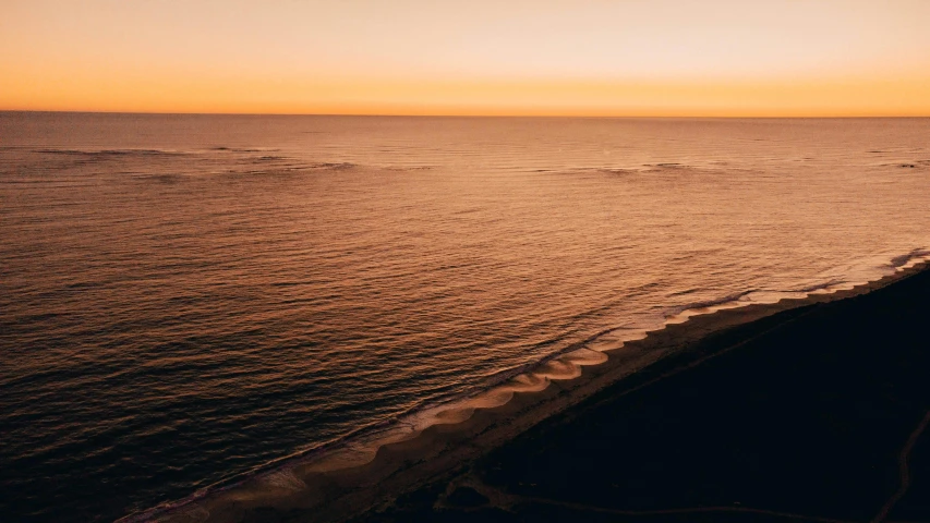 an empty beach sits on the edge of the water at sunset