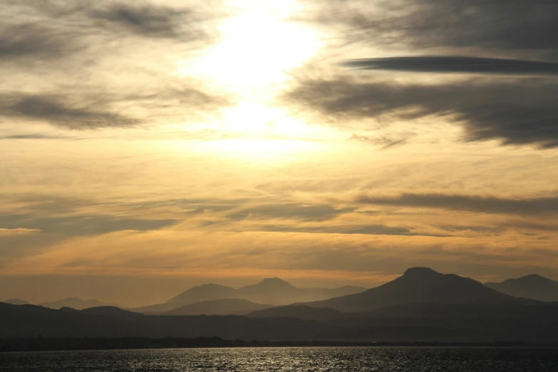 a sun setting in the clouds over the mountains