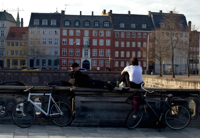 three people sit on the edge of a bridge