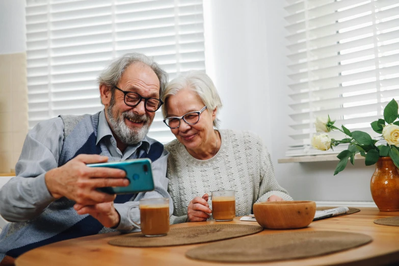 an older couple uses a cellphone at the kitchen table