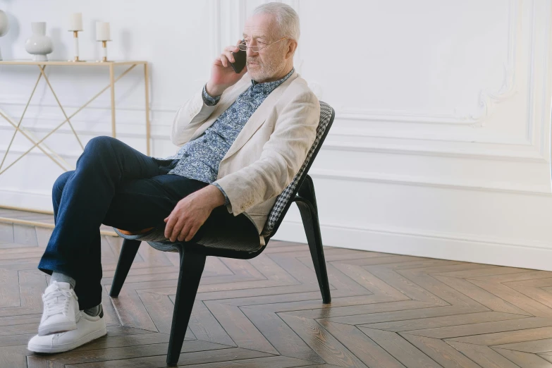 an older man sitting in a chair talking on a cell phone