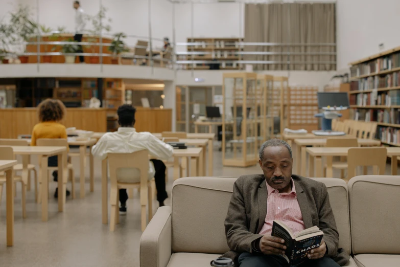 an older man reading in the liry with people sitting and reading