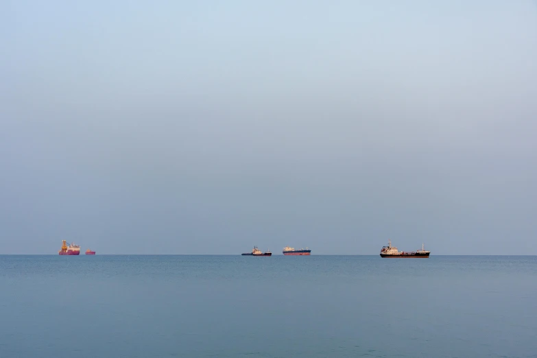 three large ships in the ocean against a gray sky