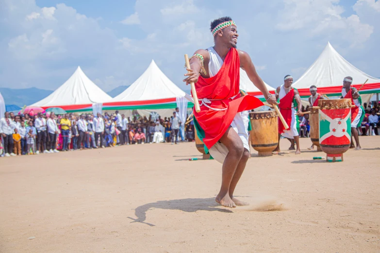 an african man wearing a colorful red blanket is dancing in the sand