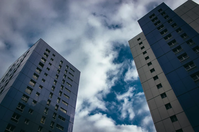 two tall buildings sit near each other in front of a blue cloudy sky