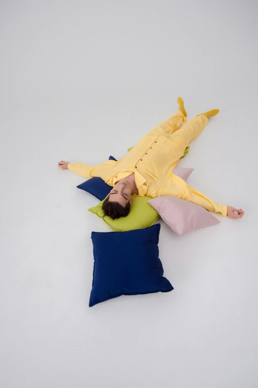 a baby in a yellow bodysuit sleeping on pillows