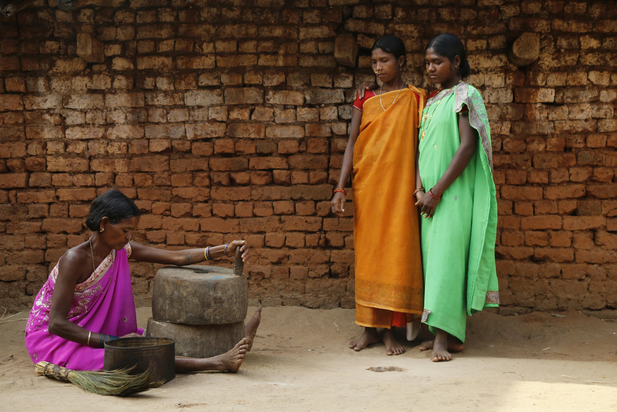 three women in green and orange dress are standing around a bucket