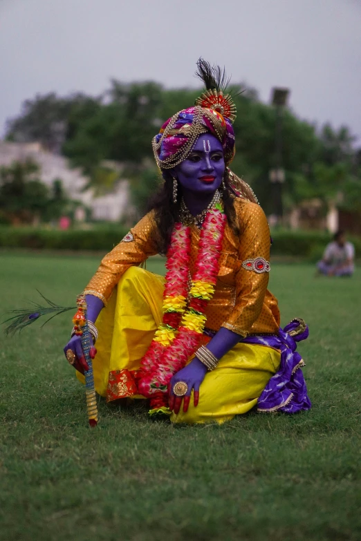 a woman dressed in bright sari and headdress is sitting in the grass