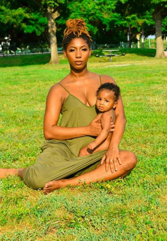 a black woman sitting in the grass holding a child