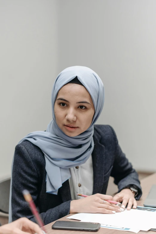 a woman with a blue hijab is sitting at a desk