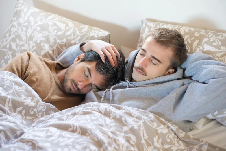 two young men laying in bed under the covers