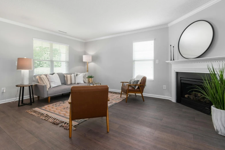 the living room with white walls, hardwood floors and two chairs, a fireplace and a mirror