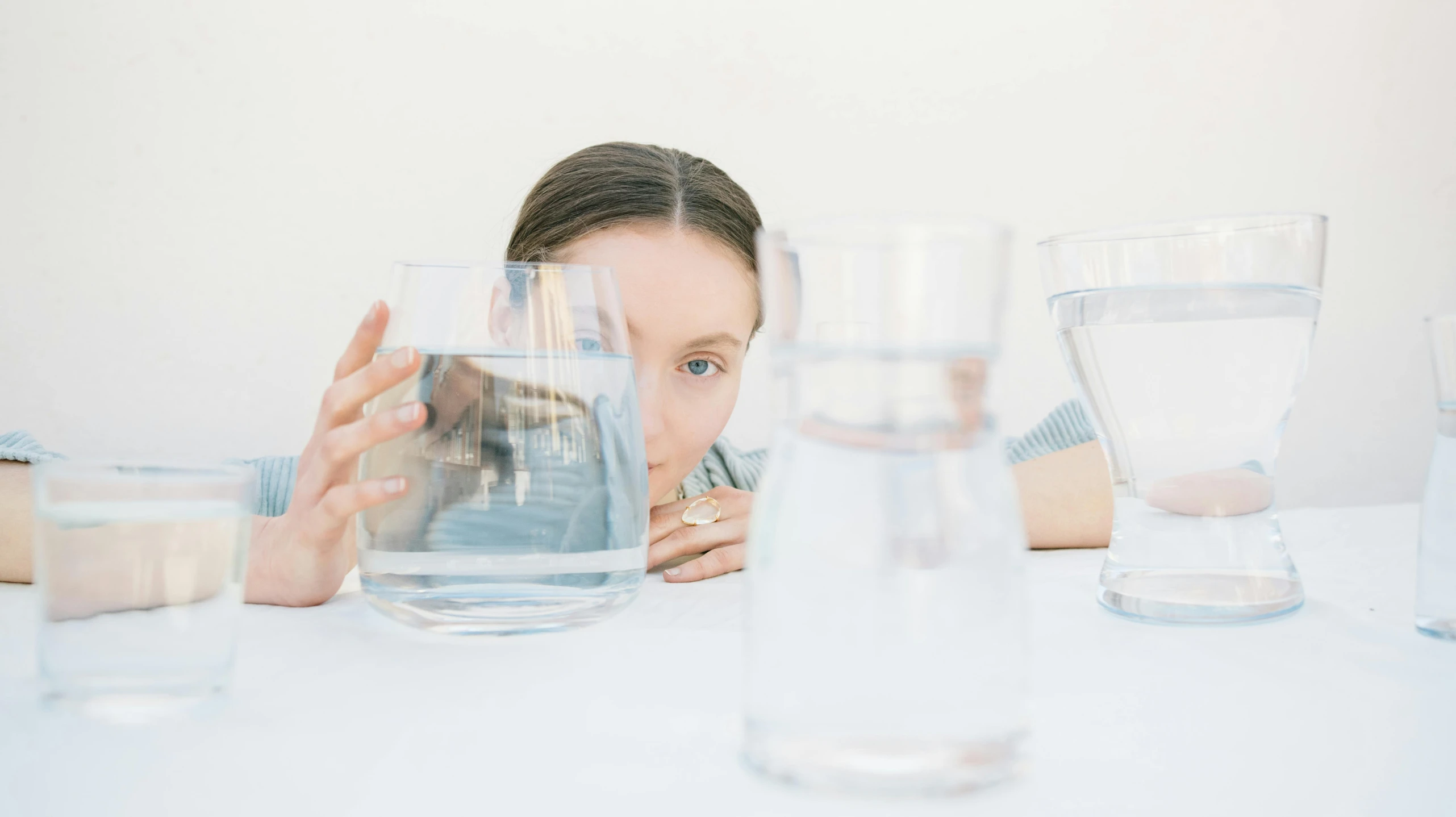 the woman sits behind many water glasses with a reflection