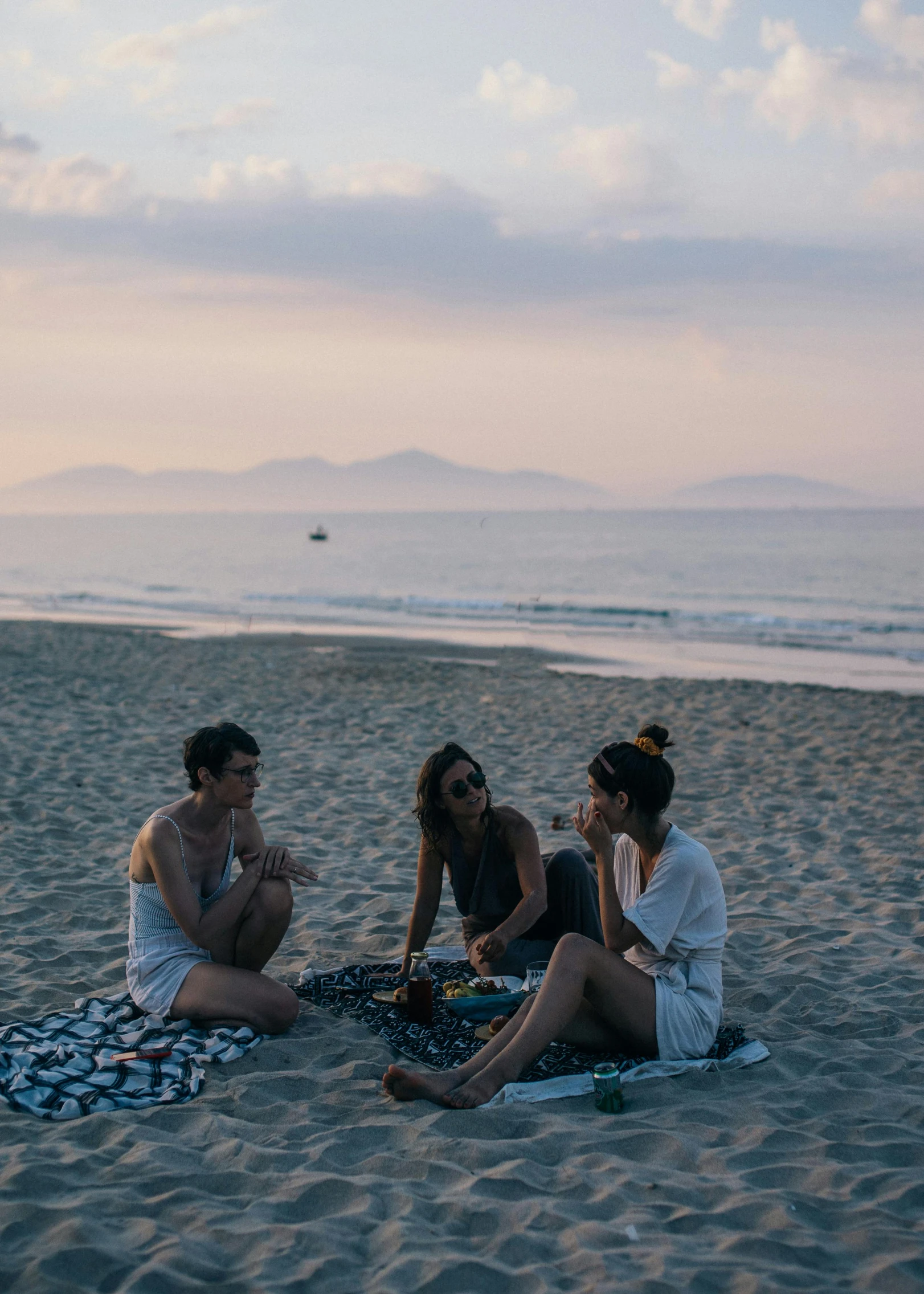 three women sitting on a blanket talking at the beach