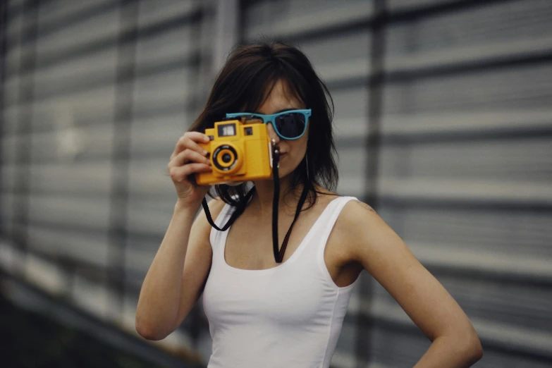 a woman holding up a camera and wearing blue sunglasses