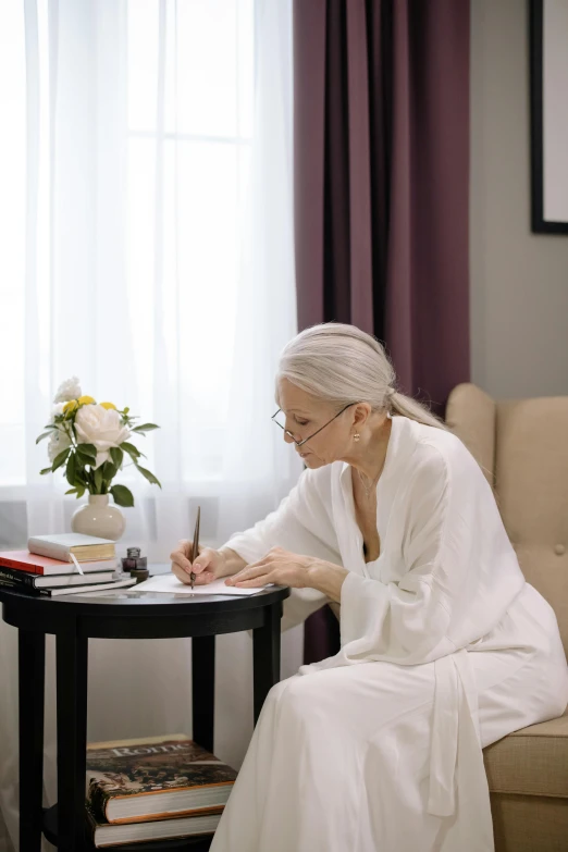 a woman is in a white robe writing with her legs crossed