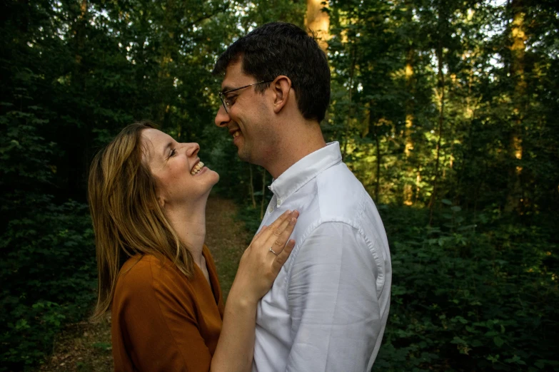 a man and woman smile at each other in the woods