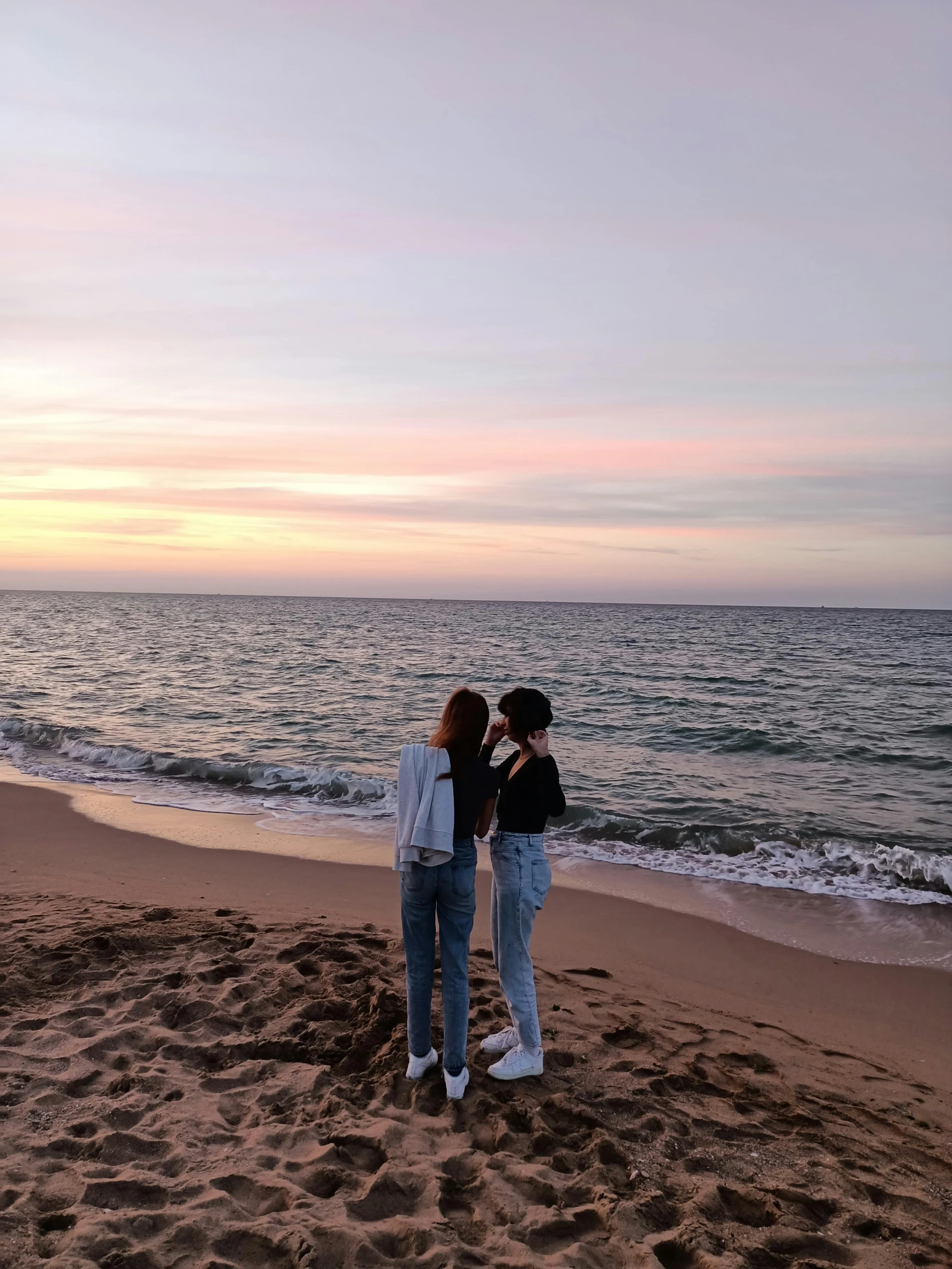 two young ladies are on the beach as the sun sets