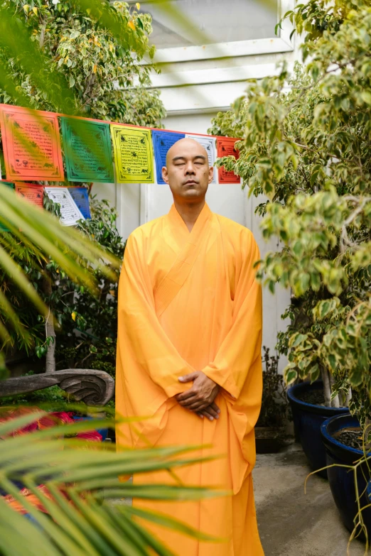 a man wearing an orange robe standing in front of green plants