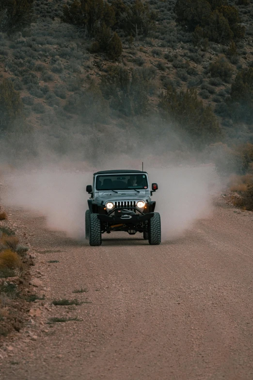 a jeep driving through the desert with dust coming out of its tires