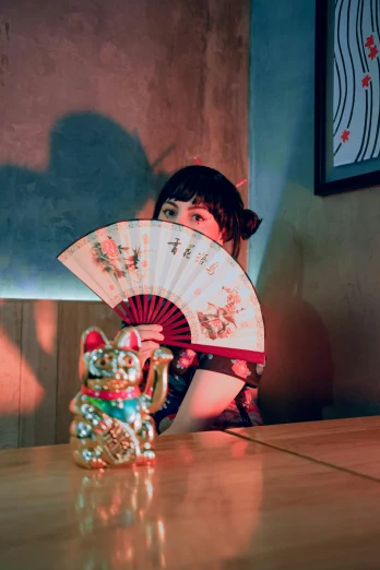 a girl is sitting on the table and she is holding up a fan