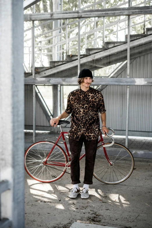 a man with a leopard print shirt and hat stands next to a red bicycle