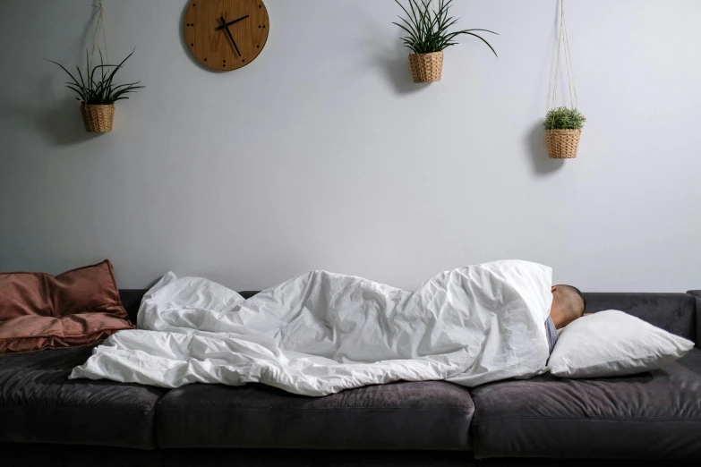 a man lying on a couch underneath three plants