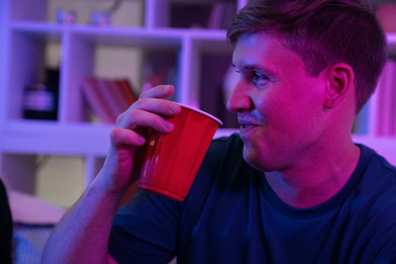 a man holding a red cup next to a book shelf