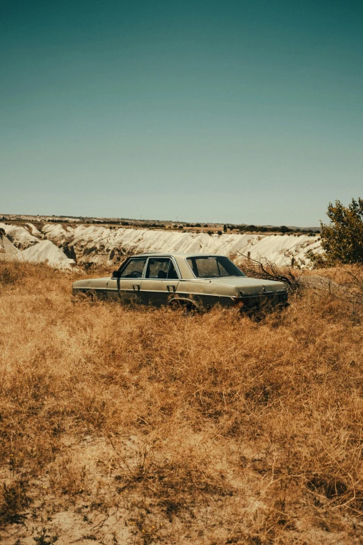 a car sits parked in tall grass by some sand dunes