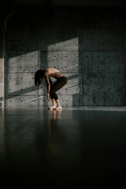 woman standing bent over on one leg near cement wall