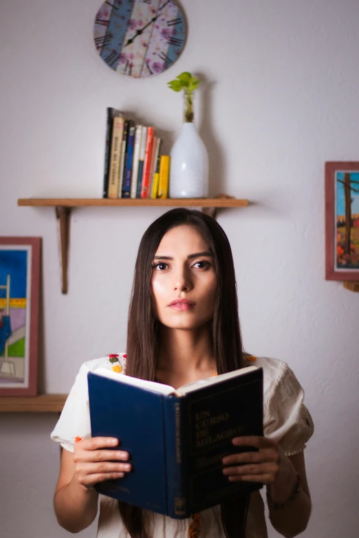 a woman is holding an open book while wearing a dress