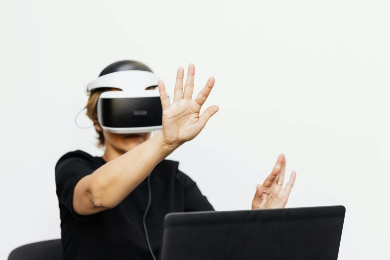 a person in a black shirt wearing a headset and wearing a laptop and holding their hand up with both hands