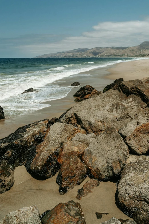 an empty surf board sitting on a rock covered beach