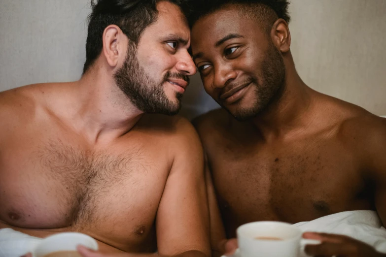 two gay men are lying in bed with mugs