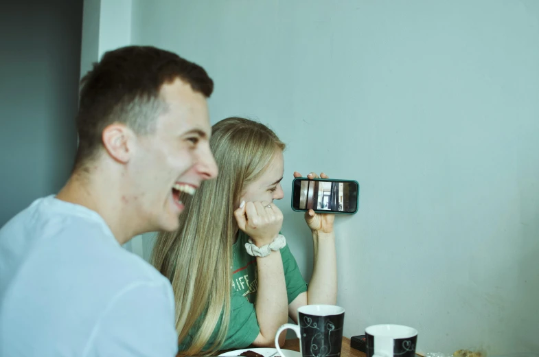 a man and a woman sit in a booth smiling as they both look at their cell phones