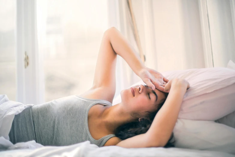 an attractive woman laying in bed next to a window