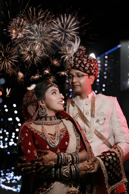 couple wearing wedding clothes and fireworks are in the background