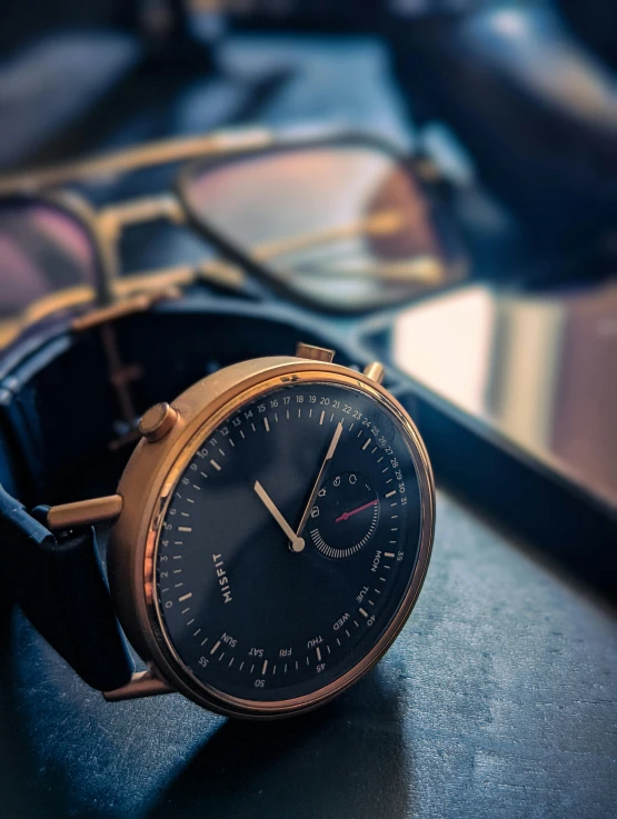 a gold wrist watch next to reading glasses