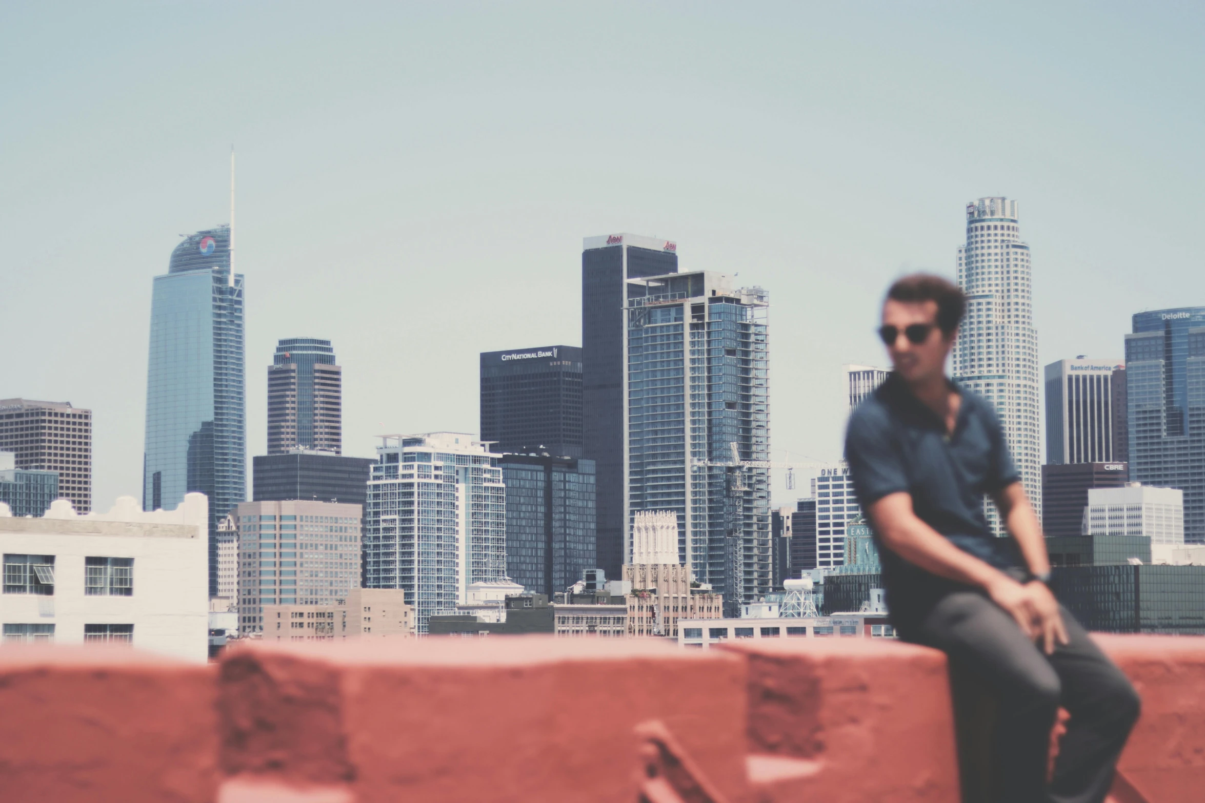 the man sits on a wall in front of the city