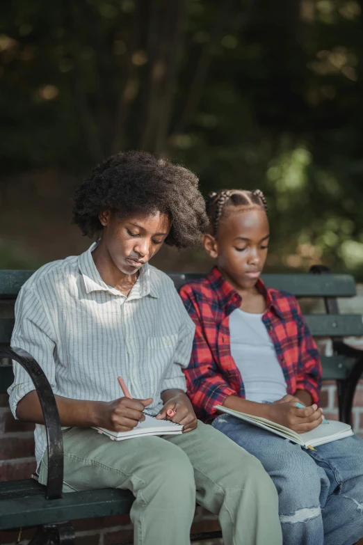 two people sitting on a bench writing with pen