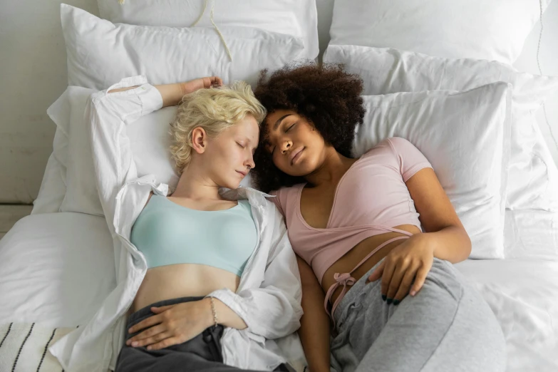 two women laying down in bed with one holding the belly of another