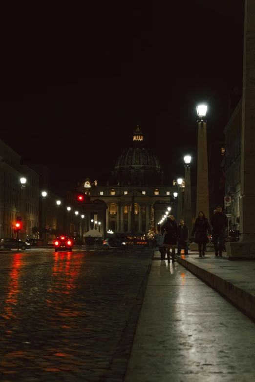 people walking down a street at night, with a building in the background