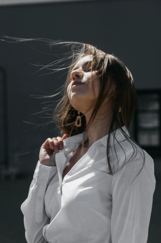 a young woman wearing a white shirt blowing her hair