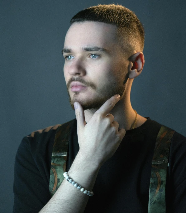 a young man wearing suspenders and a black shirt looks into the camera